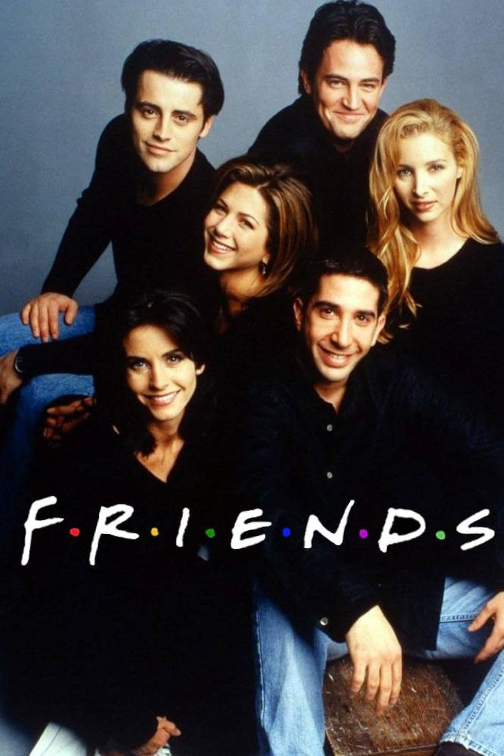Six people pose closely together, smiling, against a plain background. The word FRIENDS is written in white capital letters with colored dots between each letter across the image, capturing a moment perfect for any IPTV Latino fan.